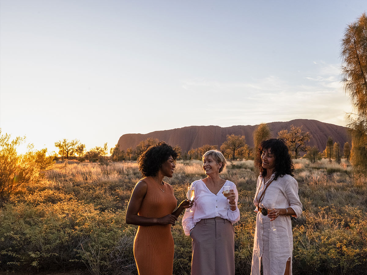 three women drinking champagne in front of uluru