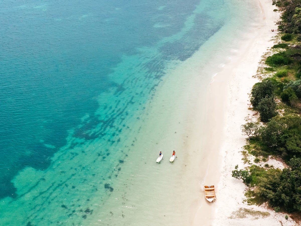 Aerial shot of two paddleboarders next to wooden row boat.